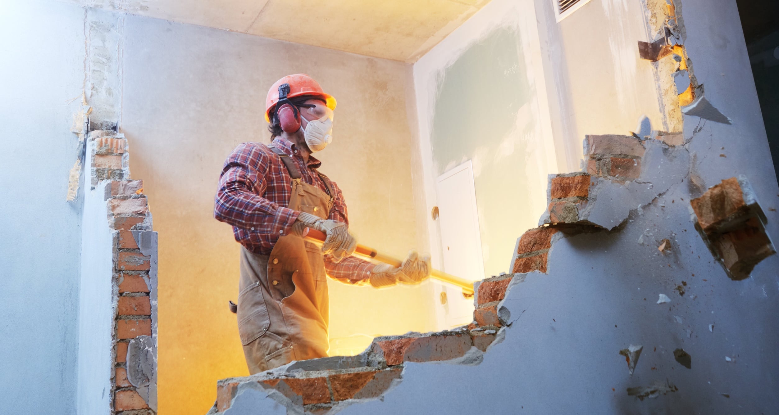 Man demolishing a wall in a home with sledgehammer